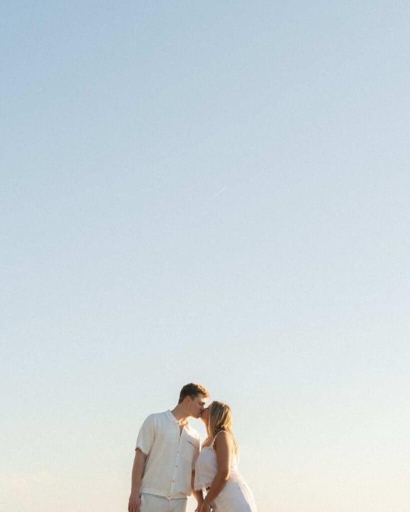couple kissing on the beach with a beautiful blue sky for their engagement photos